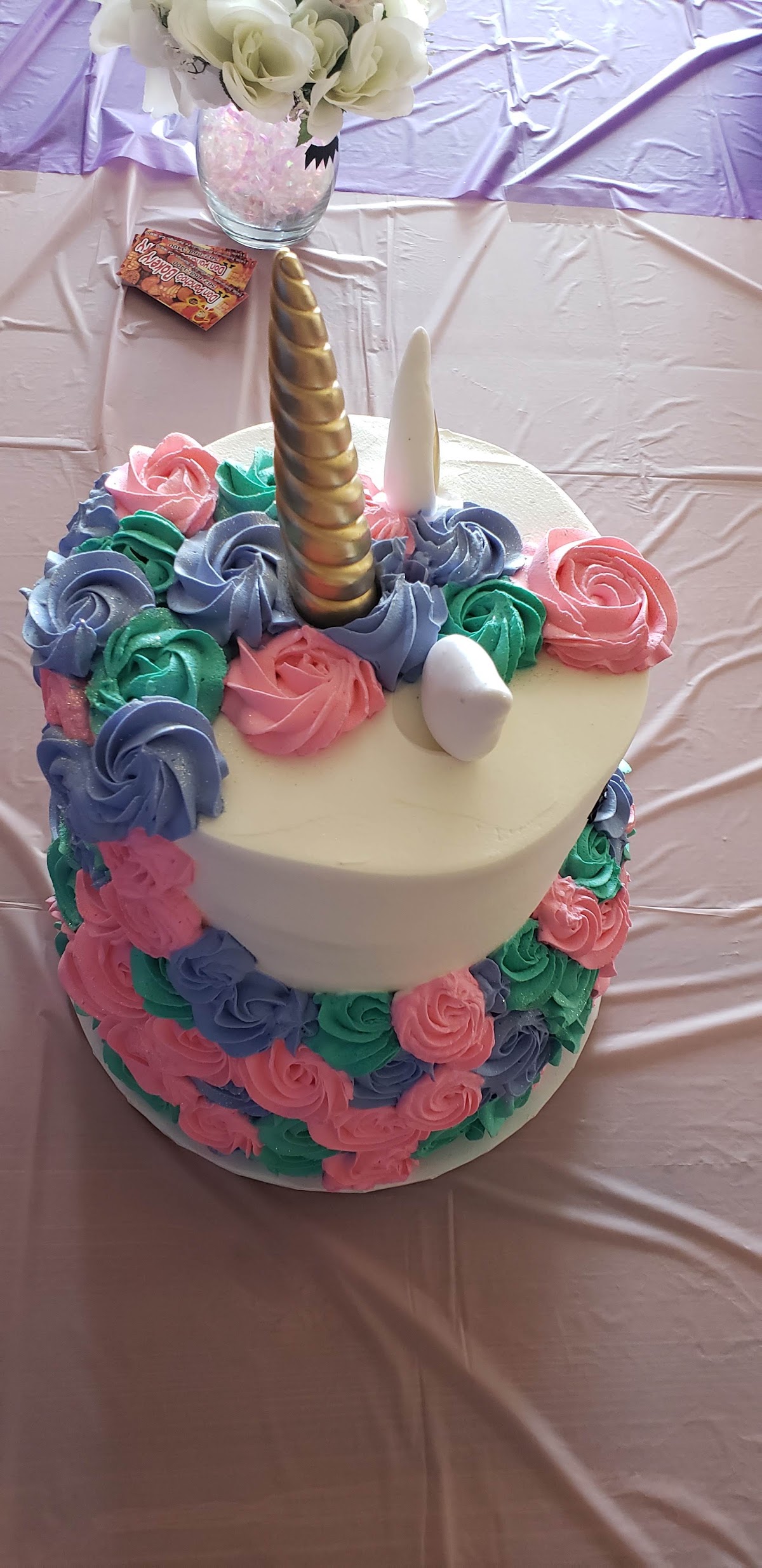 A unicorn cake in pink, teal and lilac buttercream rosettes with a gold horn